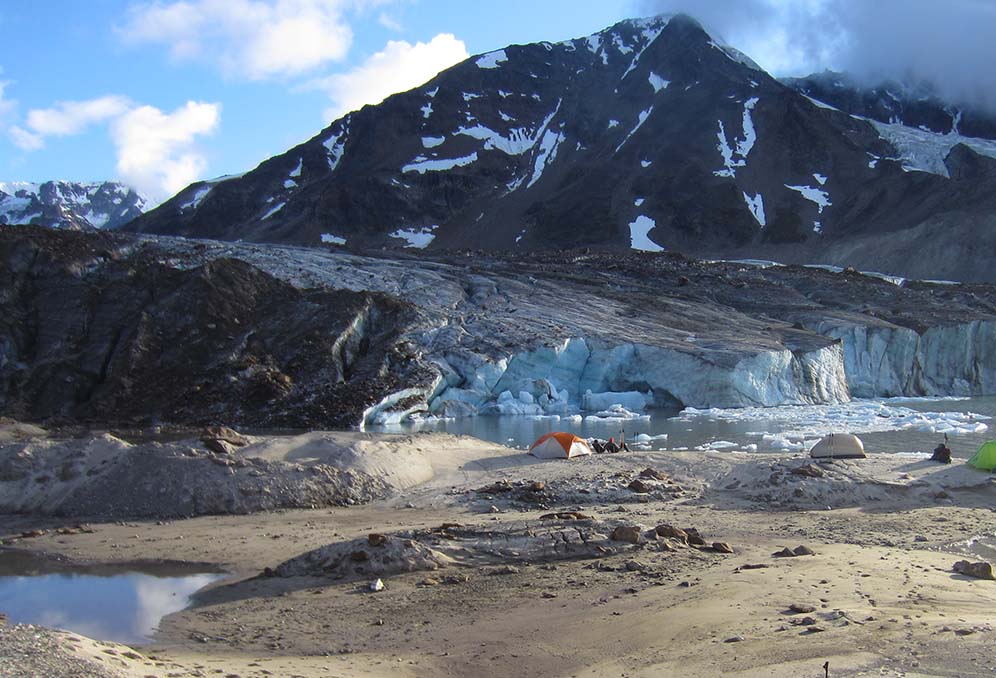 Tents set up in the sand near a blue glacier's edge