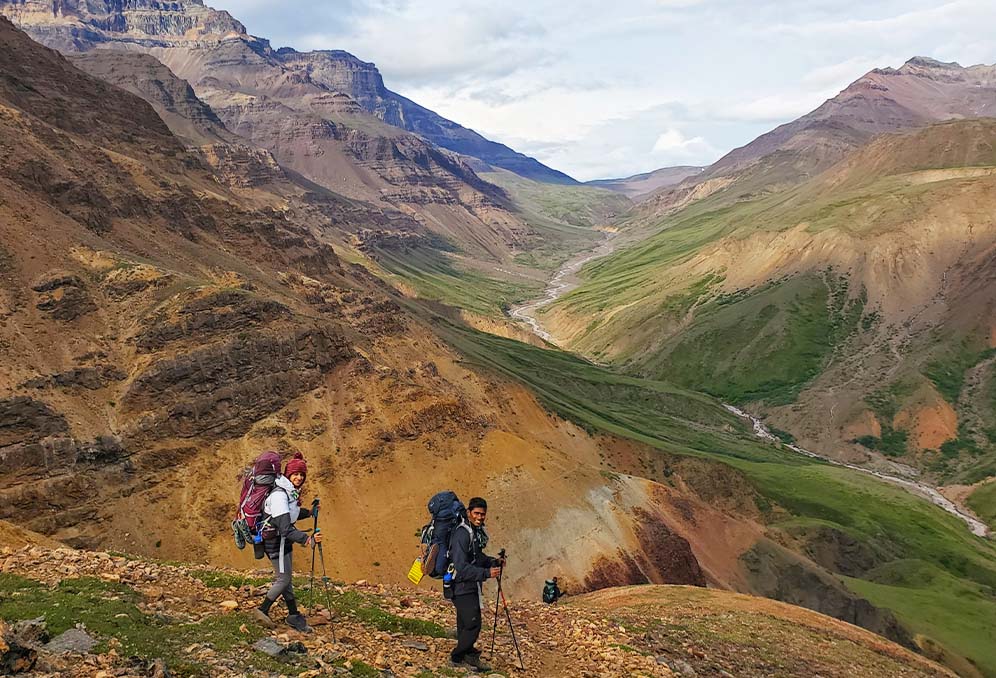 Twp backpackers stand in front of the bright orange cliffs on an epic guided trip in Wrangell - St. Elias National Park
