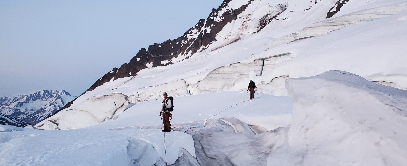 Climbers descend a snowy peak near a crevasse