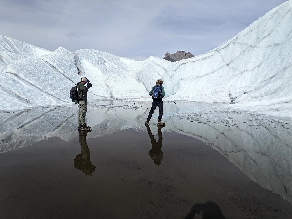 Glacier hikers step out onto a reflective pool