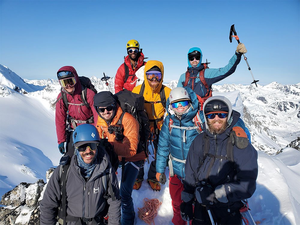 Eight excited climbers in colorful jackets on a summit in Alaska