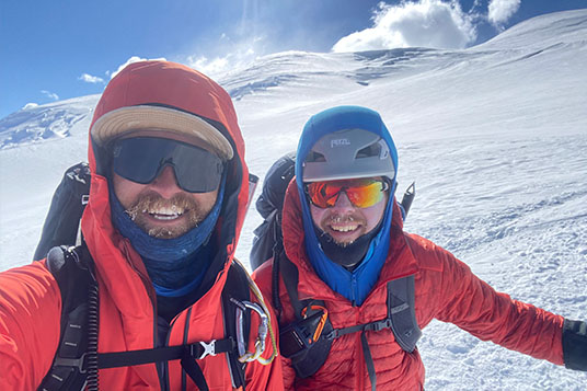 Two smiling climbers in bright jackets on a snowy slope