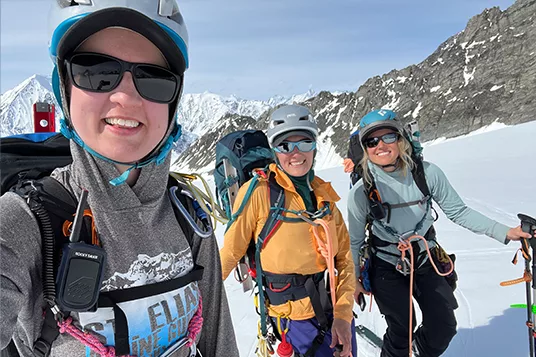 Three backcountry skiing friends smile at the camera