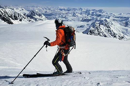 A backcountry skier in a red jacket assess his line in the Chugach Mountains