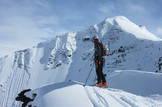 A backcountry skier looks over the edge of a peak