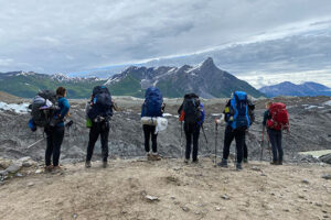 Six backpackers facing a moraine-covered glacier and mountain
