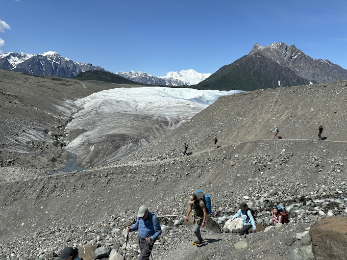 People hiking up the rocky trail with a glacier and mountains in the background
