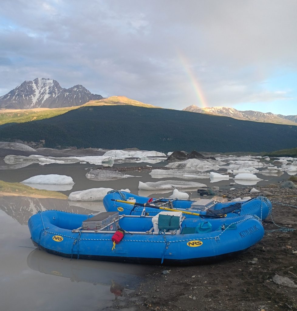 Raft in lake under mountain and rainbow