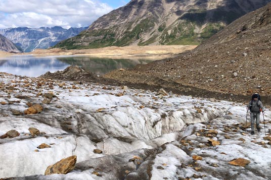 A person trekking on a glacier toward a lake