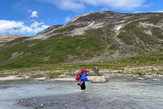 A backpacker crosses a knee-deep stream