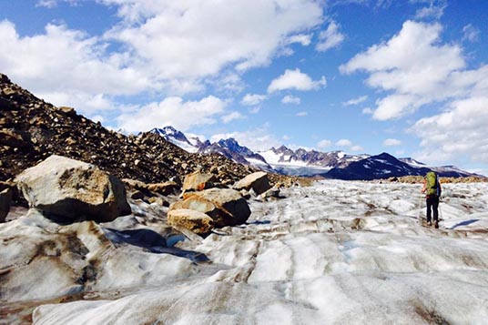 A backpacker hiking on a glacier with massive boulders