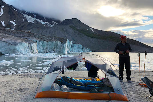A man dries his gear out in a tent at a glacier's edge