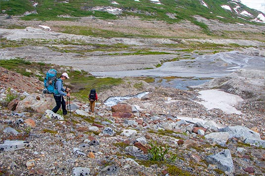 Backpackers move down a steep hill toward a river