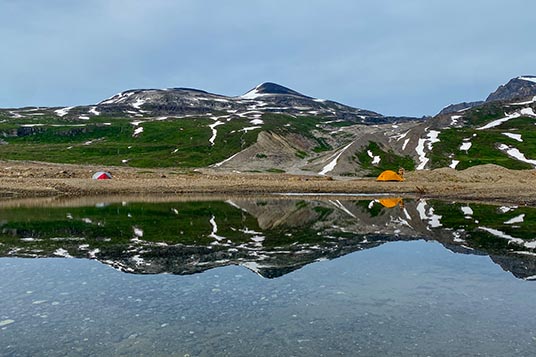 Tents set up near a backcountry lake that mirrors the mountains above