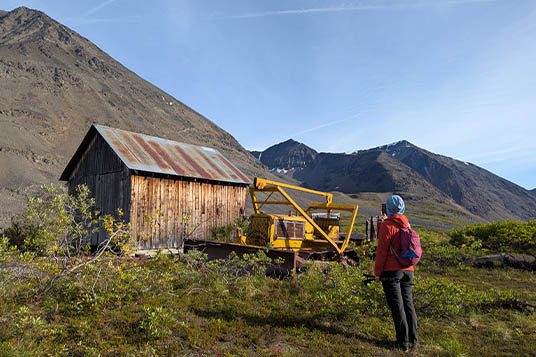 A hiker takes a picture of an old cabin and tractor in the mountains