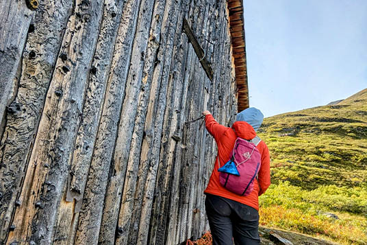 A hiker reaches to open a door of a wooden cabin
