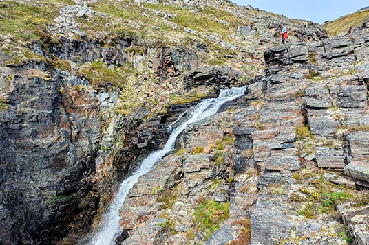 A small hiker stands over a rocky waterfall