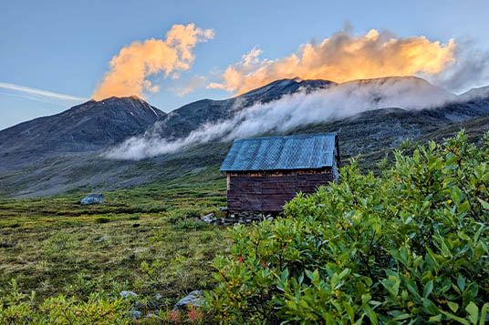 Clouds lit up by the setting sun over a small cabin