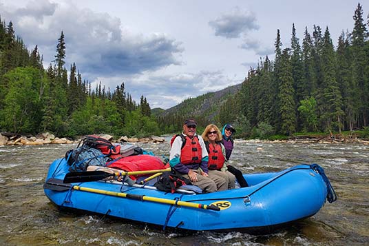 Smiling rafters in a blue raft on a river in Aalska