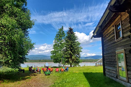 People enjoying the view of the river from camp chairs near a cabin