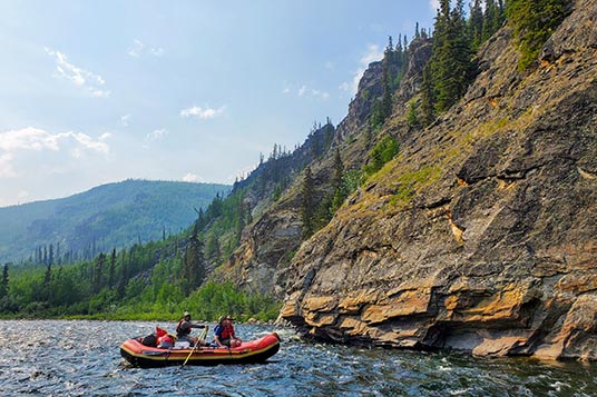A red raft coming close to a rocky outcropping