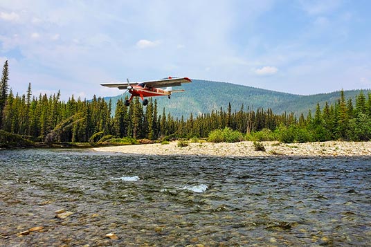 A bush plane taking off over a clear river