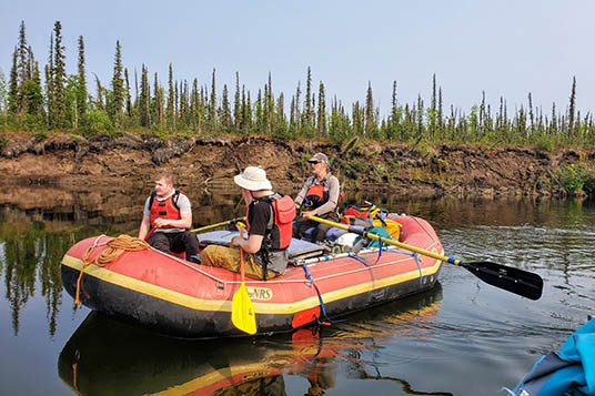 Rafters in a red boat float down clear water with muddy banks