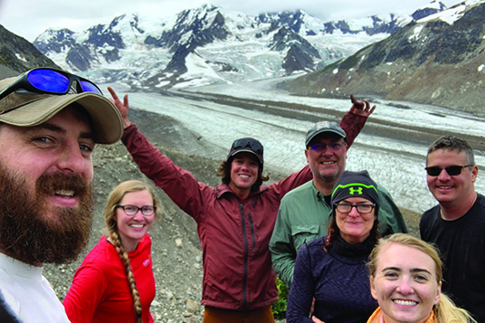A group of happy backpackers pose in front of a glacier