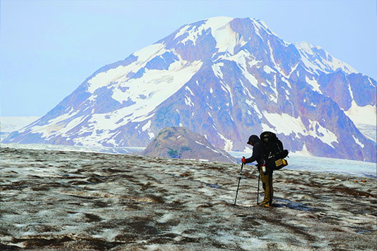 A backpacker in Alaska on a glacier with a huge mountain in the background