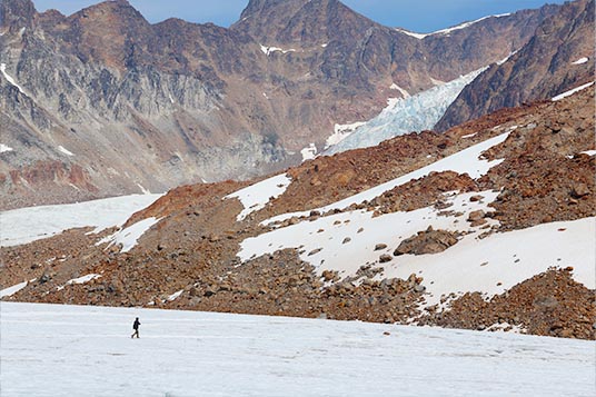 A single backpacker moves across a glacier near rocky mountains