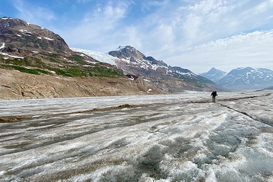 A solo backpacker walks on a flat glacier