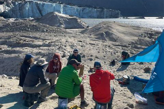 A group of backpackers lounges at camp at the glacier's edge