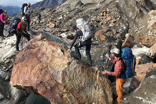 A backpacker makes her way over a large boulder with the group's help