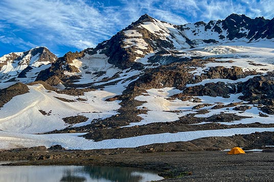 A yellow tent beneath a large glaciated peak