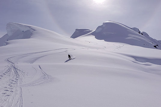 A skier coming down a wide slope with a cornice
