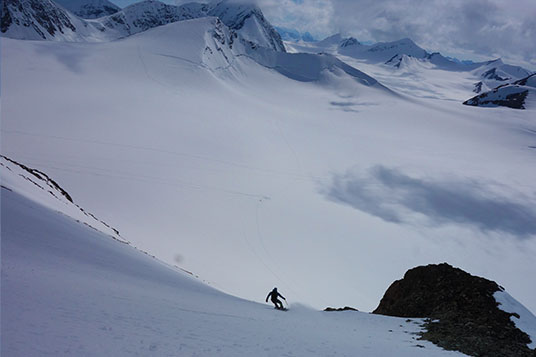 A splitboarder riding down a big slope in the Chugach Mountains