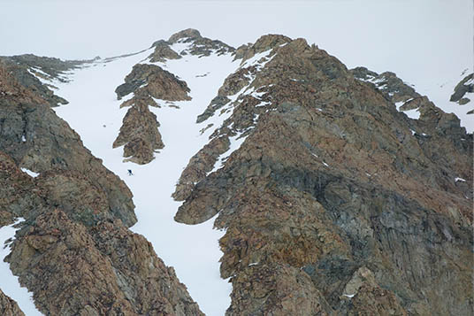 A tiny skier in a narrow couloir on a rocky face
