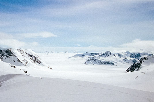 A tiny skier gives a sense of scale to an enormous white landscape of snowy mountains