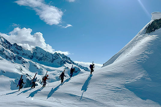A group of backcountry skiers with skis on their packs ascent a summit
