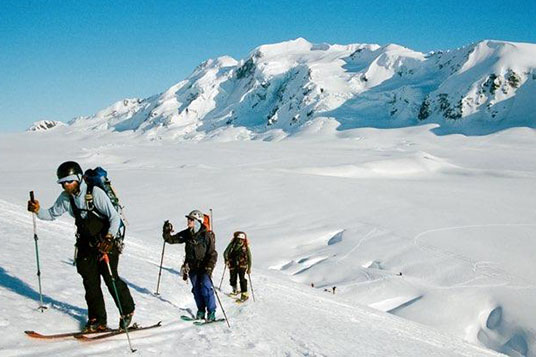 Backcountry skiers ascent a mountain from a snowy glacier