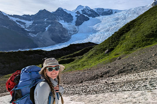A hiker smiling at the camera with the Stairway Icefall towering behind her