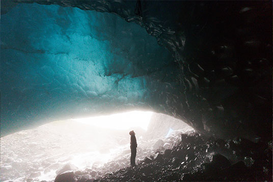 A person in a glowing blue ice cave in Wrangell - St. Elias National Park