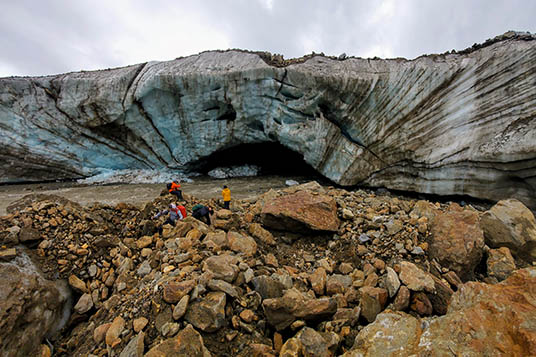 Hikers approach an ice cave in a glacier in Wrangell - St. Elias National Park