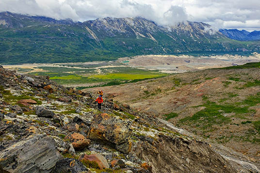 A hiker in a red jacket on a rocky slope in the Chugach Mountains