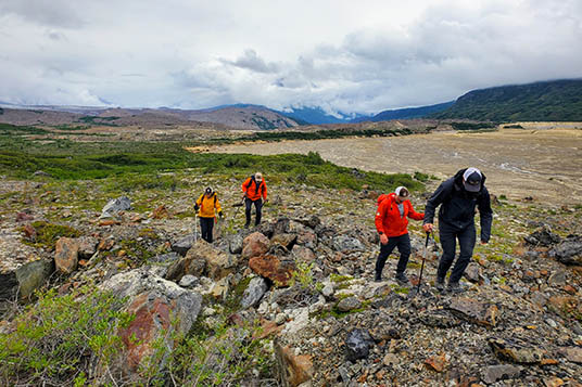 Hikers walk up a rocky hill near the Fan Glacier