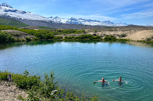 Two people swim in a blue alpine lake
