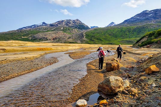Alaskan hikers walk on the sand near a shallow creek