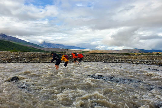 Four hikers in bright jackets ford a shallow river