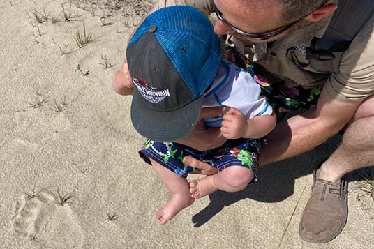 Man holds baby over a bear print in the sand
