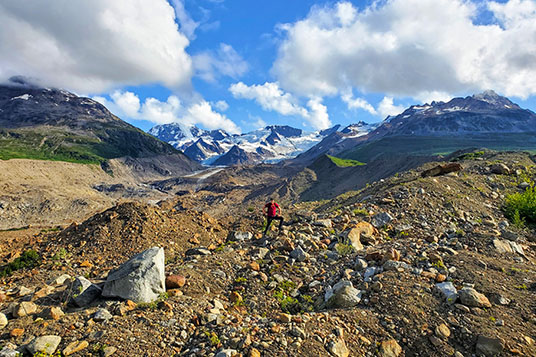 A hiker on a rocky slope in front of glaciated peaks